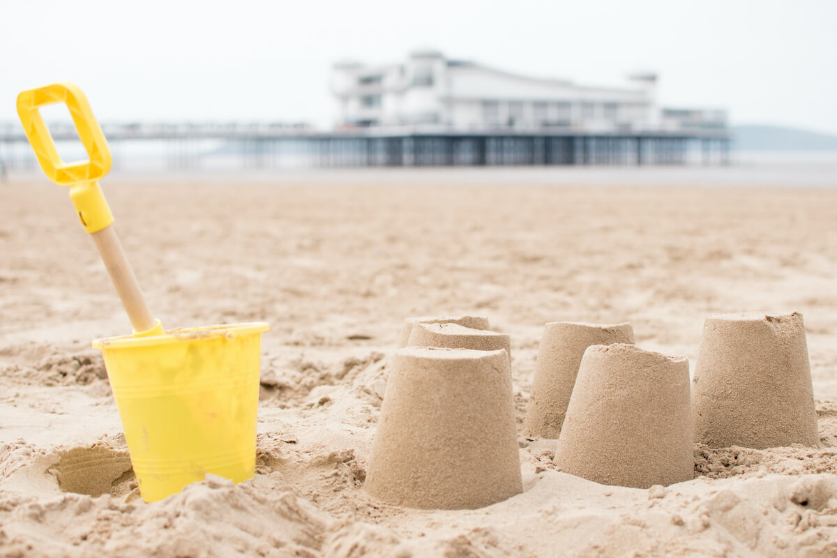 Sand castles on the beach with a pier in the background